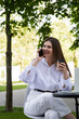 © MM - A woman in a white shirt and white pants sits at a table in a street cafe and talks on the phone.