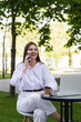 © MM - A woman in a white shirt and white pants sits at a table in a street cafe and talks on the phone.