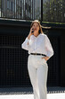 © MM - A woman in a white shirt and white pants speaks on the phone
