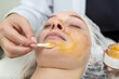 beautician applying golden facial mask on a young female face client