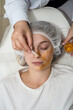cosmetologist applying gold facial mask by brush on face female client at spa