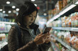 © Victor Bertrand - Woman using smartphone in grocery store with soft focus background.