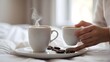 © Ashan - a close-up of a woman's hand gently holding a cup of just brewed morning coffee against a background of peaceful, white, soft, and clean bed linens