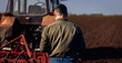 Rear view of mature farmer standing in field looking at tractor while cultivate the land.