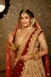 © Sudip - Stunning Indian bride dressed in traditional bridal lehenga with heavy gold jewellery and veil smiles tenderly in studio lighting. Wedding fashion and lifestyle.