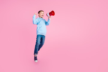 Wall Mural - Full body profile portrait of beautiful little boy jump raise fist communicate loudspeaker empty space isolated on pink color background