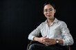 Portrait of an asian business woman entrepreneur politician student teacher coach sitting on chair looking on camera wearing eyeglasses white shirt isolated on black background
