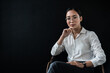 Portrait of young asian beautiful businesswoman entrepreneur politician student teacher coach sitting front black background. Woman looking at camera and keeping hand on chin while posing