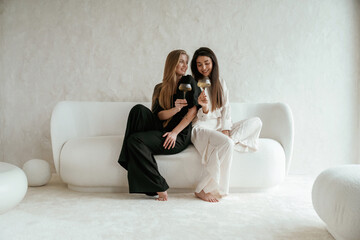 Event, with drinks, celebrating. Two happy young female best friends are indoors