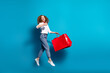 Photo portrait of nice young lady jump shopping bags show thumb up wear trendy white garment isolated on blue color background