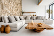 Live edge wooden coffee table near grey sofa. Wild stone cladding wall and white wall with shelves in spacious room. Minimalist interior design of modern living room, home.