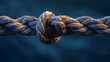 © JuroStock - Closeup of an old rope with two loose ends tied together, symbolizing strength and connection, against dark blue background