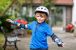 Portrait of little school kid boy in safety protection clothes scating with rollers. Active sporty child doing sports on summer day. Outdoor activity for kids.
