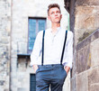 Young European guy in shirt and trousers with suspenders walking around city
