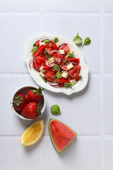 Wall Mural - Watermelon salad in a bowl with lemon and strawberries on a white background