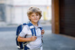 Happy little kid boy with backpack or satchel called Ranzen in German. Schoolkid on way to school. Portrait of healthy adorable child outdoors. Student, pupil, back to school. Elementary school age