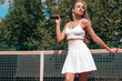 Young beautiful woman wearing fashionable white dress skirt and tank top. Hot model posing on tennis court at summer sunny day. Sexy female stands near net