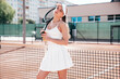 Young beautiful smiling woman wearing fashionable white dress skirt and tank top. Hot model posing on tennis court at summer sunny day. Sexy female stands near net, cheerful and happy