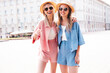 Two young beautiful smiling hipster female in trendy summer clothes. Sexy carefree women posing on street background. Positive models having fun, hugging. In hat
