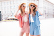 Two young beautiful smiling hipster female in trendy summer clothes. Sexy carefree women posing on street background. Positive models having fun, hugging. In hat