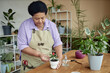Waist up portrait of Black senior woman repotting green plant with care and enjoying gardening at home, copy space