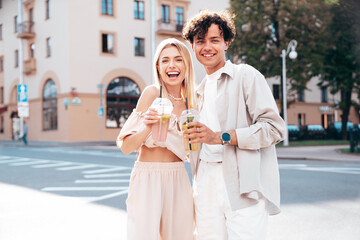 Wall Mural - Young smiling beautiful woman and her handsome boyfriend in casual summer clothes. Happy cheerful family. Female having fun. Couple posing in street. Holding and drinking cocktail drink in plastic cup