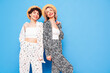 Two young beautiful smiling brunette hipster female in trendy summer costume clothes. Sexy women posing near blue wall in studio. Positive models having fun. Cheerful and happy, in hat