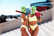 Two beautiful sexy women in green underwear. Models wearing bandit balaclava mask. Hot seductive female in nice lingerie posing in the street at sunny day, blue sky. Crime and violence. Perfect body