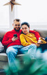 Positive couple in love watching video online on smartphone using wifi connection at home interior,romantic marriage resting on comfortable sofa viewing common photos on mobile phone at leisure
