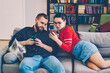 Positive male and female hipster couple viewing common pictures on smartphone sitting on sofa,young marriage share multimedia content via mobile phone and wireless connection at home interior