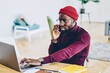 Concentrated african american hipster guy talking on mobile phone while doing remote work on laptop computer, dark skinned male checking banking balance making telephone call and browse website