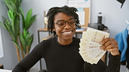 Sticker - Cheery young black woman with dreadlocks basking in success at office, confident smile showing teeth while holding danish krone banknotes, positive and delighted