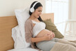 Happy pregnant woman with headphones listening to mozart music and lying on bed, pregnancy concept