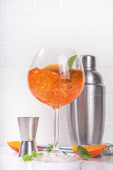 Wall Mural - Classic italian aperitif aperol spritz cocktail in glass with ice cubes, alcohol sweet long alcohol drink with slice of orange and mint, on white background with hard light and bar utensils