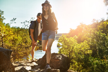 Nature, hiking and couple walking with river, blue sky and adventure holiday in countryside. Trekking, man and woman on sustainable travel vacation together in park with trees, water and outdoor date