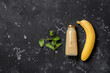 Banana juice in a bottle and fresh banana on a black stone background. Top view, flat lay,