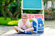 Happy little kid boy with glasses sitting by desk and backpack or satchel