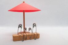 Model Safety Pin Of Family Sitting On Wooden Block With Red Umbrella Background. Family Insurance Concept
