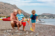 Happy grandfather and two little kid boys playing together on beach and building sand and stone castle. Beautiful family enjoying vacations on sea and ocean, granddad and children