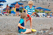 Two little blond kids boys building pebble stone castle on beach. Funny siblings, children playing with bucket and shovel. Vacations, summer, travel concept. Twins enjoying summer vacations on sea.