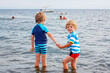 Two little blond kids boys having fun by taking bath in ocean or sea. Funny siblings, children holding hands. Vacations, summer, travel concept. Twins on Mediterranean Sea