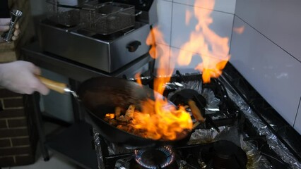 Wall Mural - A man is cooking food in a wok on a stove. A chef is cooking food in a pan with a lot of fire.