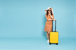 Happy young Asian woman traveler with luggage isolated on sky blue background, Tourist girl having cheerful holiday trip concept, Full body composition