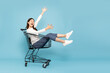 Happy young Asian woman sitting inside of shopping trolley isolated on blue sky background, Wow and surpise concept
