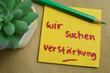 Concept of Wir suchen verstarkung write on sticky notes isolated on Wooden Table.