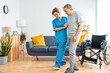 Young caregiver assisting senior man in wheelchair walking indoors - Home health care service and physiotherapy concept