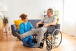 Young caregiver assisting senior man in wheelchair indoors - Home health care service and physiotherapy concept