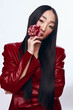 Stylish woman with long black hair in red leather jacket holding pink flower portrait