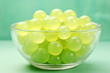 A glass bowl filled with green chewing jelly candies on teal background macro shot. Sweet snack dessert