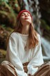 © Andrea Marongiu - Tranquil woman meditates outdoors, her features softened in relaxation against a blurred natural waterfall background, exuding a peaceful vibe with her eyes closed and wearing comfortable clothing